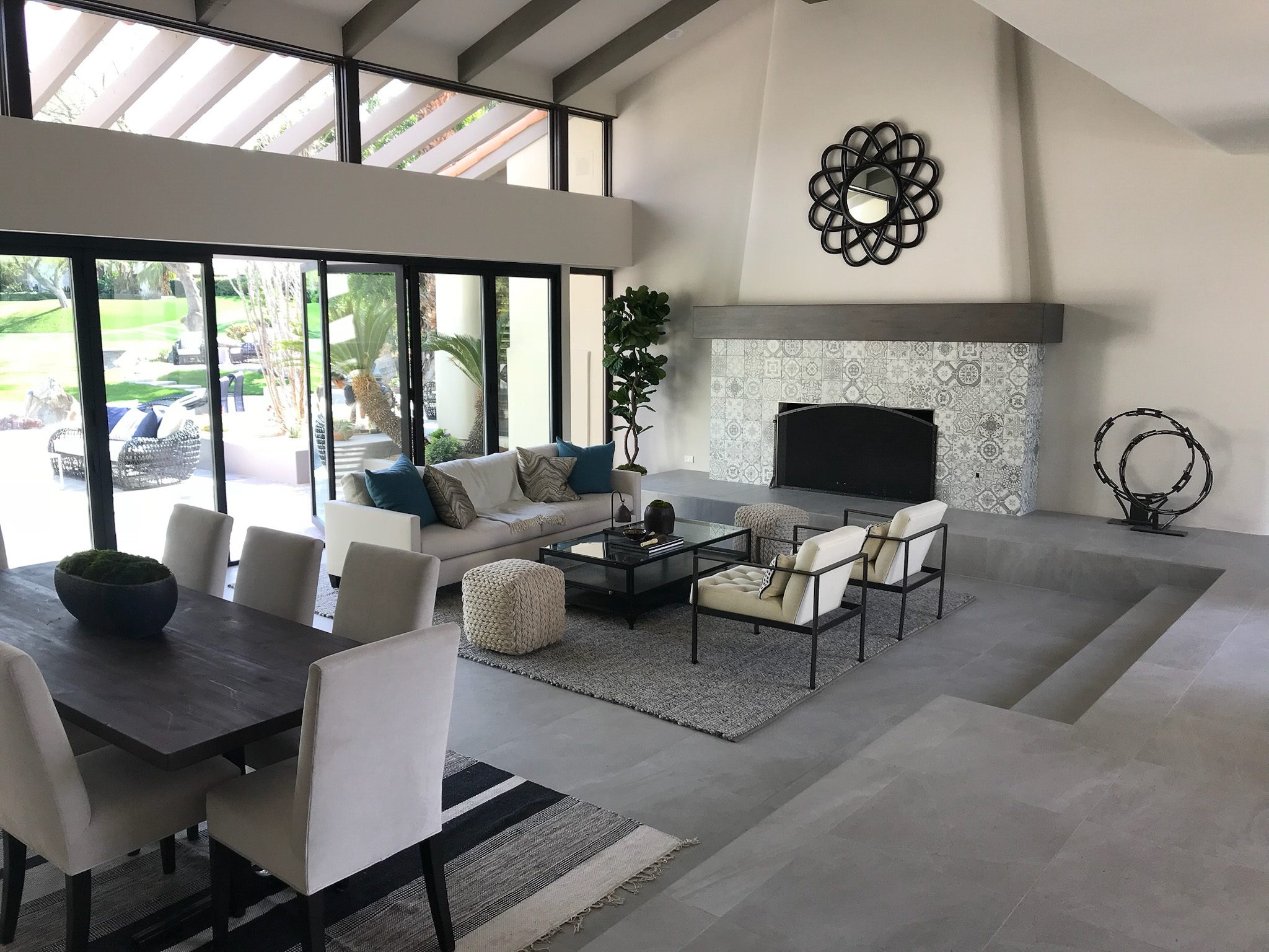 Spacious living room with a modern design, featuring a fireplace, large sofas, and a dining area, overlooking a lush garden.